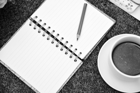 Dramattic moment .Have a cup of black coffee.Writing on copy space note book . with Pencil on grass Background.With selective focus.の写真素材