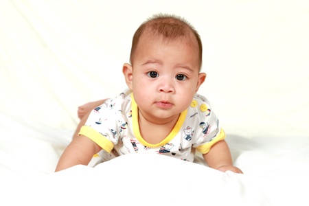 Cute baby boy in bathrobe crawling in bed against white backgroundの写真素材