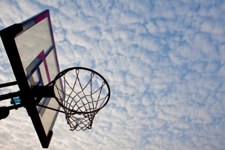 A view of a basketball hoop from below, sky and clouds.