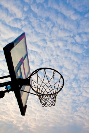A view of a basketball hoop from below, sky and clouds.の写真素材