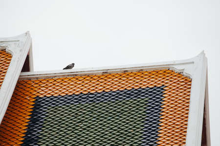 A bird is on multiple roof tiers of the Thai templeの写真素材