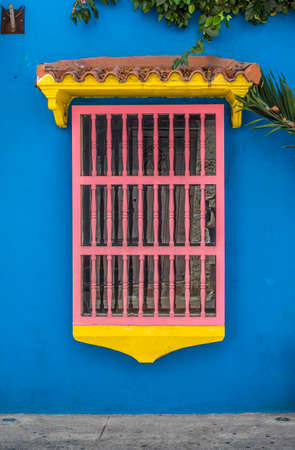 Facade of a blue colonial house with a pink / yellow window in the old center of Cartagena de Indias in Colombia, South Americaの写真素材