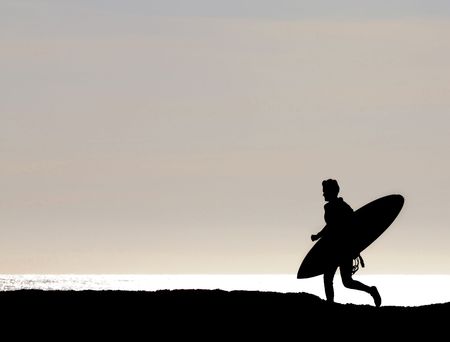 Surfer sihouetted while running along cliff at Santa Cruz Point to get the last few waves before sunsetの写真素材