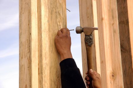 Hispanic carpenter pounding a nail in with a framing hammer at a house under constructionの写真素材