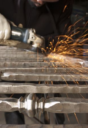 Blacksmith working on decorative handrail applying finishing grinding to the welds