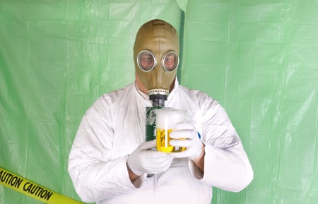 Man in Hazmat clothing in temporary green plastic decontamination chamber wearing a gas mask and carrying toxic chemical that is exuding gaseous vaporの写真素材