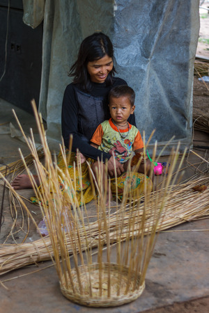 SIEM REAP, CAMBODIA - 9/12/2015: A mother takes a break from making baskets to relax with her child.のeditorial素材