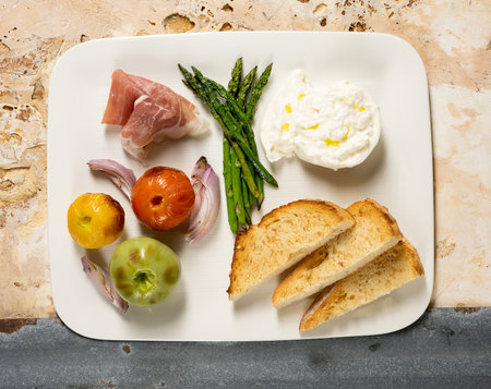 Appetizer plate above view with poached egg, prosciutto, onions, asparagus, bread, tomatoes on an above viewの写真素材