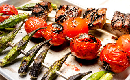 Grilled okra, cherry tomatoes and pork skewers close-up on a trayの写真素材