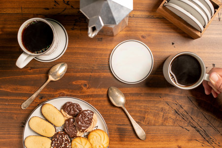 Fresh coffee with biscuits and hand holding mug with spoons on a wooden tableの写真素材