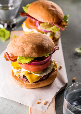 Freshly prepared cheeseburgers on serving platter with bacon, lettuce, tomatoes, onion and picklesの写真素材