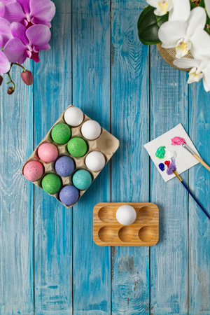 Multicolored easter eggs on blue table with paint brushes and paintの写真素材