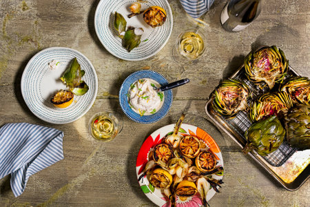 Grilled artichokes and yogurt dipping sauce with bottle of wine, two glasses filled, above viewの写真素材