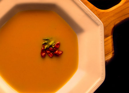 Pumpkin soup in bowl on wooden board topped with garnishの写真素材