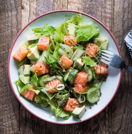 Fresh salmon salad with cucumbers, avocado, lettuce, arugula, white onions, pepper in bowl on wooden tableの写真素材