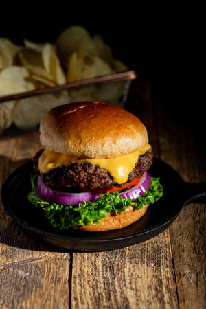 Dark and moody fresh hot cheeseburger with brioche bun and potato chips in the backgroundの写真素材