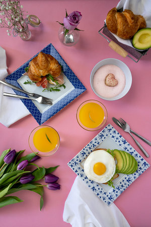 Top view of a brunch table setting with food. Beautiful pink background and fresh flowers
