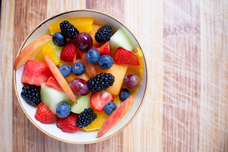Bowl of fresh cut fruit on a wooden cutting board with sunlight to the rightの写真素材