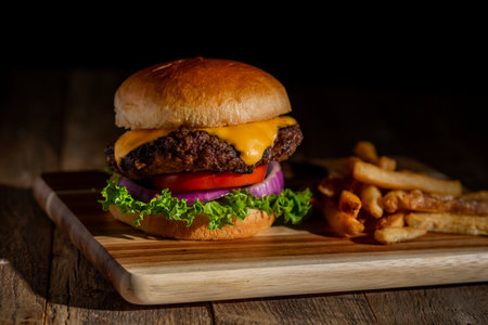 Hot hamburger with melting cheese, lettuce, tomato with french fries on a cutting boardの写真素材