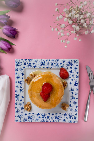 Plate with a small stack of pancakes, strawberries, walnuts and syrup. Surrounded by roses and flowers.の写真素材
