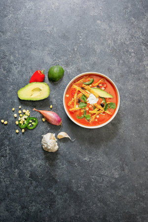 Chicken tortilla soup in bowl on black background with vegetablesの写真素材