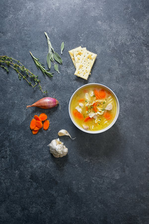 Chicken noodle soup in bowl on black background with vegetablesの写真素材