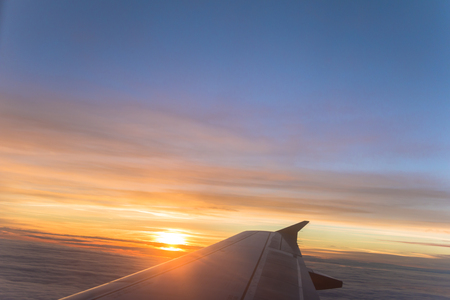 Airplane Window view of airplane wing and sunrise sunset over orange and blue sky.の写真素材