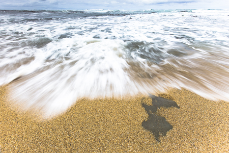 Ocean sea water rushing in to sandy beach shore on a cloudy blue sky.の写真素材