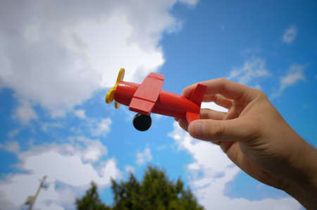 Hand flying a red toy airplane against a blue sky.の写真素材