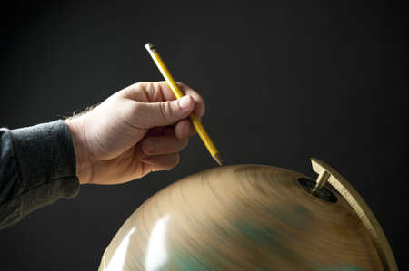 A hand holding a pencil and pointing at a spinning globe.の写真素材