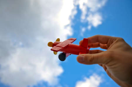 A hand flying a red toy plane against a blue sky.の写真素材