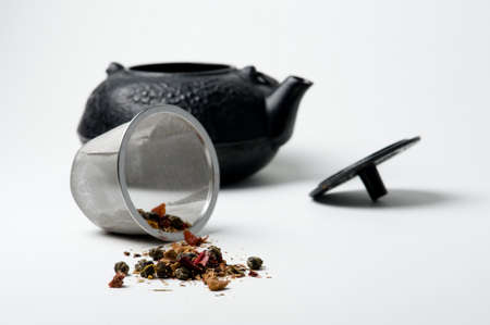 Close up of a teapot and spilled tea leaves against white. の写真素材