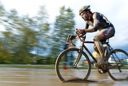 A muddy, energized, and determined cyclocross racer riding through a mud puddle.の写真素材