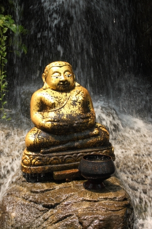 Golden Prosperity Buddha sat on the stone at waterfall, Thailandの写真素材