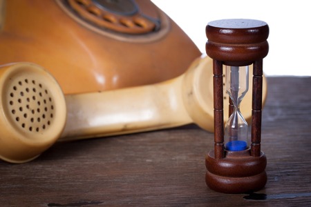Hourglass and old telephone on wood table.