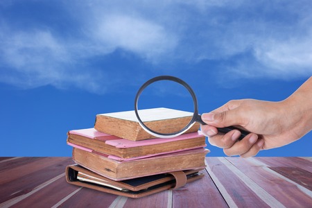 Hand holding magnifying glass over book with blue skyの写真素材