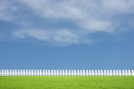White fences on green grass with blue skyの写真素材