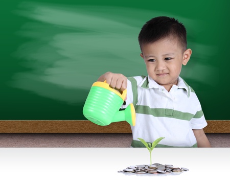 Little boy watering the small green plant growing out of coinsの写真素材