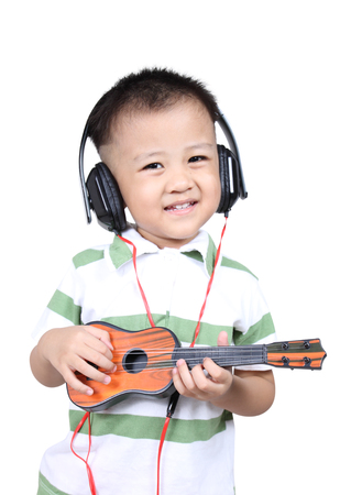 Happy Kid palying ukulele guitar with headphones , isolated on white backgroundの写真素材