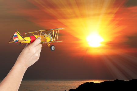 woman's hand holding toy airplane at orange sunset, Travel conceptの写真素材