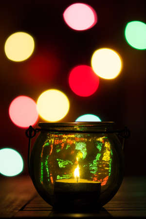 Lamp made of a glass vase with a candle at night. Christmas decoration with colored lights in the backgroundの写真素材