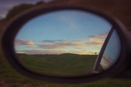 Sunset landscape seen in the rearview mirror of a car, on country roadの写真素材