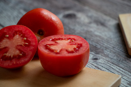 A halved tomato on a chopping board. Everything sits on a rustic gray table. Near the table are other tomatoes. night lightの写真素材