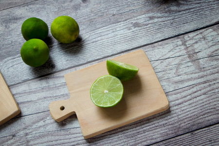 green lemons on a cutting board. one of the lemons is split in half. all on a rustic gray table.の写真素材