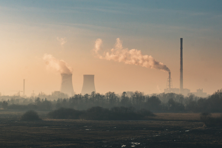 Landscape with field and trees, in the distance factory and a power station, with the factory pipes going smoke against the yellow sky, Severe pollution of the environmentの写真素材