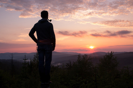 The guy with the Smoking pipe looking at mountainous landscape at sunsetの写真素材
