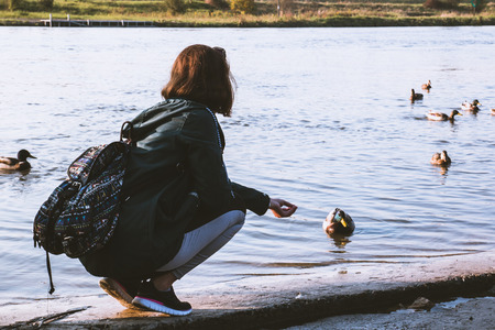 Young girl feeding the ducks on the lake in the springの写真素材