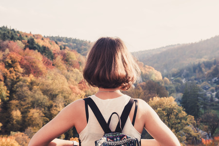 Young beautiful girl with backpack looking at autumn mountain landscapeの写真素材