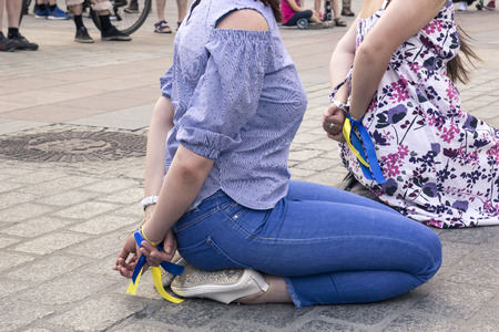 Two women with their hands tied behind their backs sit on their knees in the city square, a social protest against repression and the prohibition of freedom of speechの写真素材