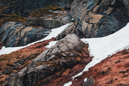 Snow lies on the ground in the mountains among the red grass and large stonesの写真素材